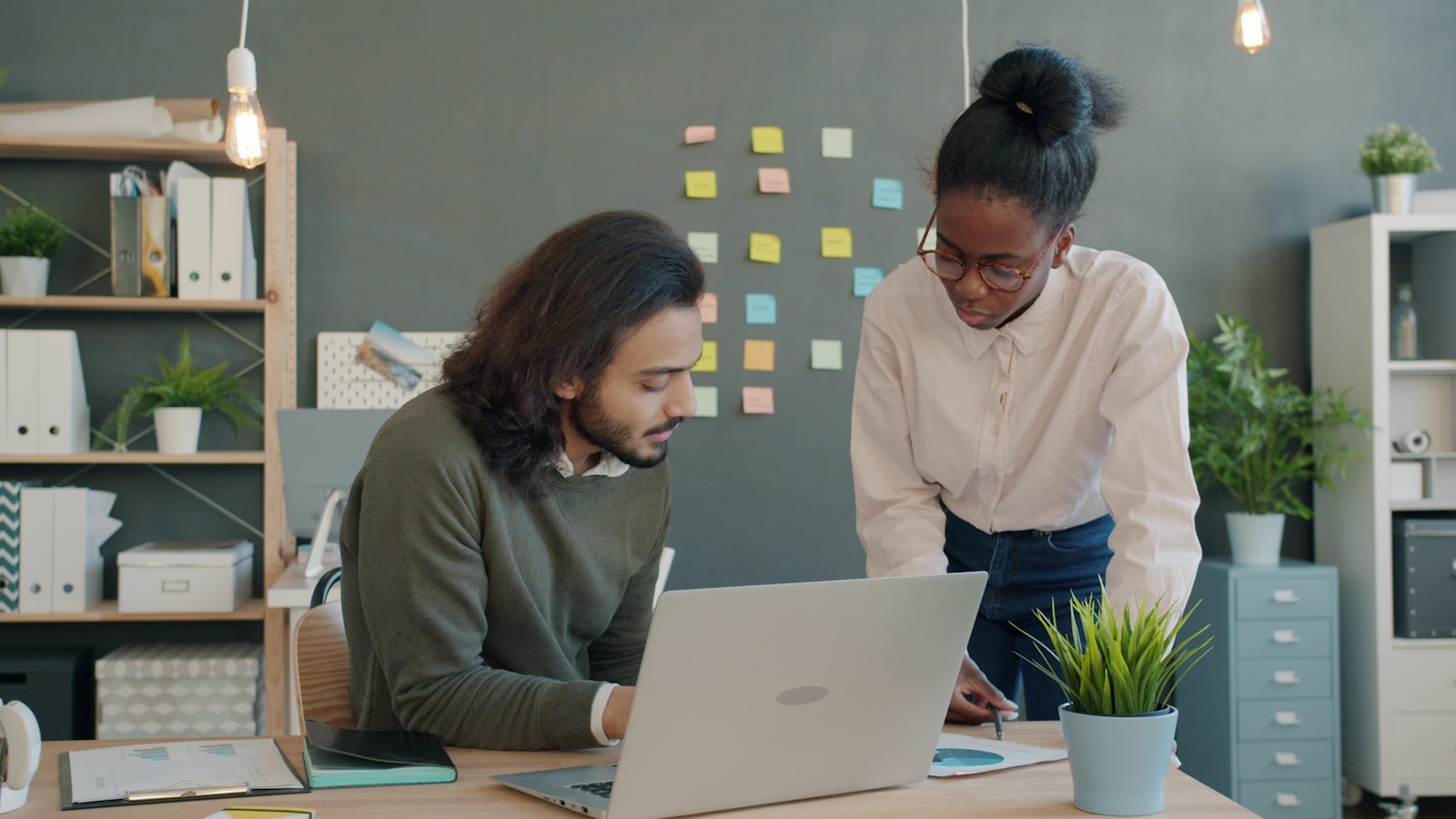 Two colleagues reviewing documents beside a laptop