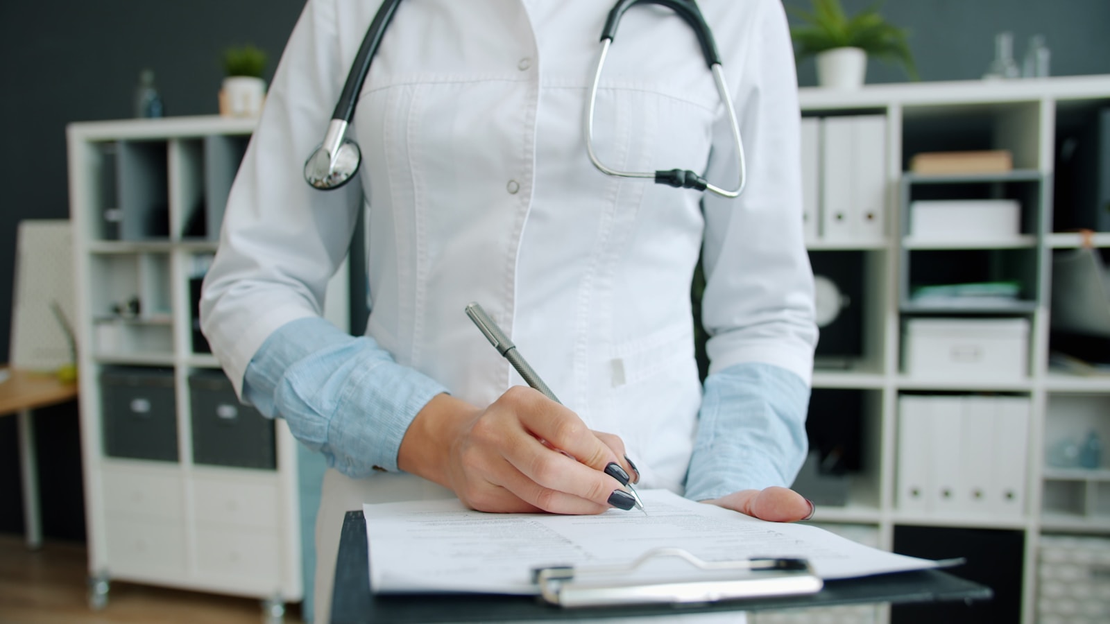 Medical practitioner completing paperwork beside a stethoscope